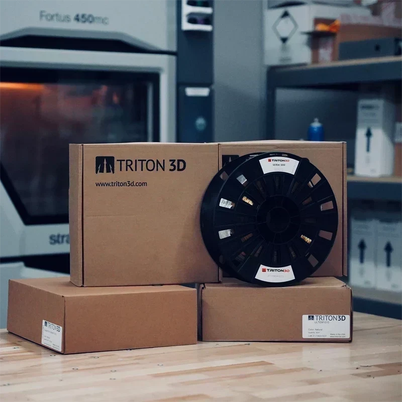 Triton3D ULTEM 1010 filament spool and boxed spools in front of a Stratasys Fortus 450mc 3D printer